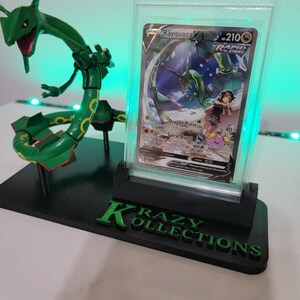 May include: A green and white Pokemon card featuring Rayquaza, a dragon-like Pokemon, in a clear plastic protective case. The card is on a black display stand with the words "Krazy Kollections" in green letters.