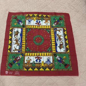 May include: Red cotton bandana with a Christmas theme. The bandana features a repeating pattern of nutcrackers, reindeer, and a wreath. The bandana is made in the USA.