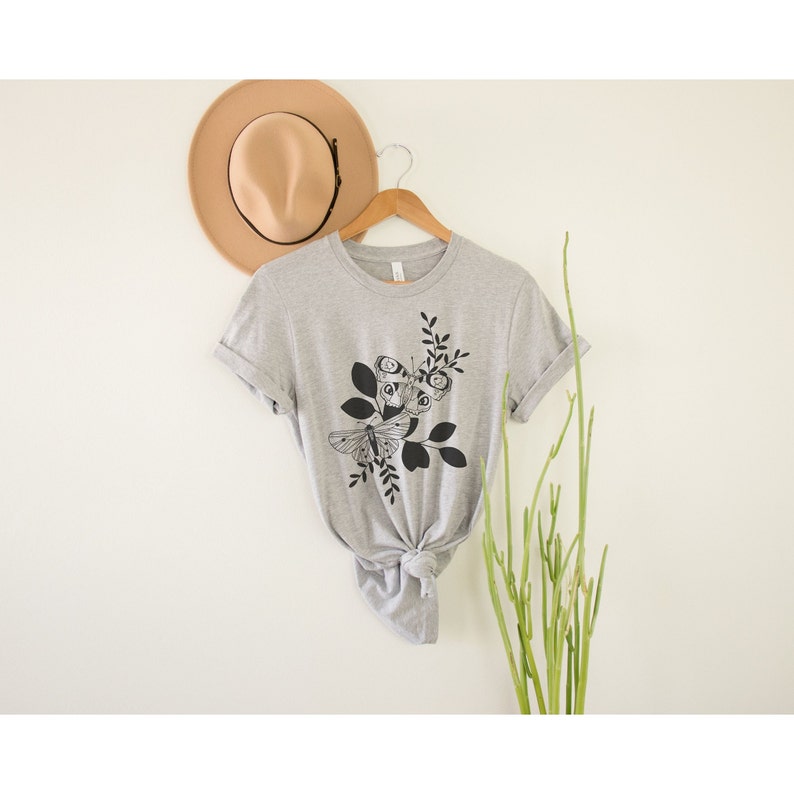 May include: A gray t-shirt with a black and white graphic of butterflies and leaves.