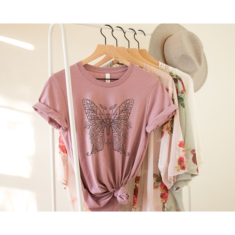 May include: A mauve t-shirt with a black and white mandala-style butterfly graphic.