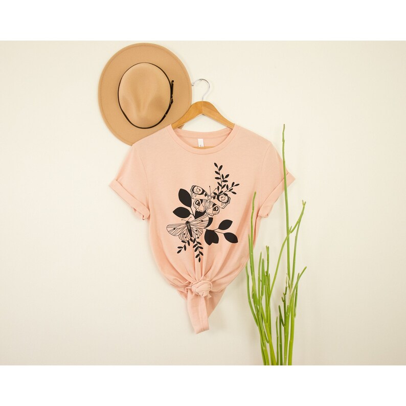 May include: A peach-colored t-shirt with a black and white graphic of two butterflies on a branch with leaves.