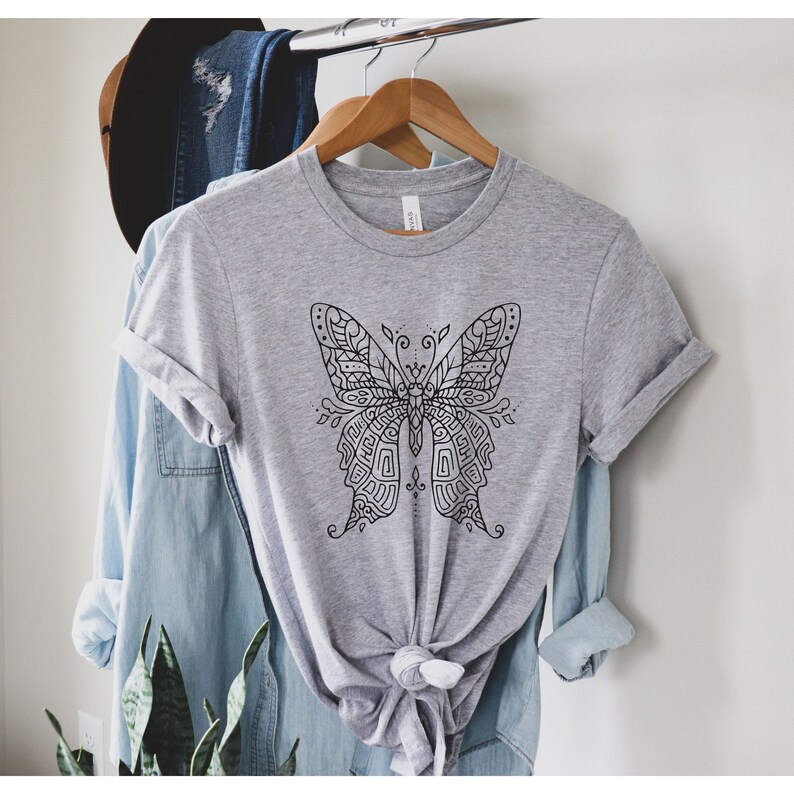 May include: A gray t-shirt with a black and white intricate butterfly design.