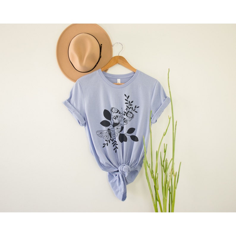 May include: A light blue t-shirt with a black and white graphic of butterflies and leaves.