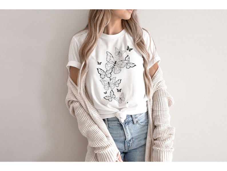 May include: A white t-shirt with a black and white butterfly design. The butterflies are arranged in a cluster, with the largest butterfly at the top and the smaller butterflies cascading down.