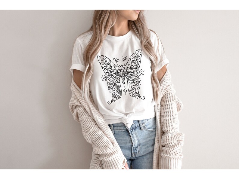 May include: A white t-shirt with a black and white intricate butterfly design. The butterfly is centered on the shirt and has a detailed pattern.