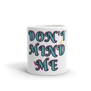 Puede incluir: Taza de cerámica blanca con el texto "DON'T MIND ME" en letras azules y rosas. El texto está en un estilo de fuente retro.