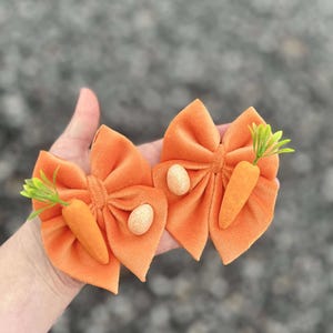 May include: Two orange velvet hair bows with a carrot and a glittery egg embellishment.