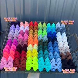 May include: A tray filled with a variety of colorful hair bows. The bows are arranged in rows, showcasing a spectrum of colors from pinks and purples to greens and blues. The text "BLACK ROCK CREATIONS" is visible in multiple places.