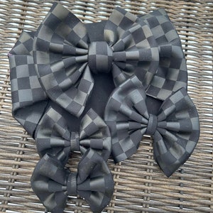 May include: Four black and white checkered fabric hair bows of varying sizes. The bows are arranged in a pyramid shape, with the largest bow at the top and the smallest bow at the bottom.