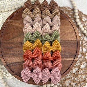May include: A collection of corduroy hair bows in various colors, including brown, pink, green, yellow, orange, and rose. The bows are arranged on a wooden tray, showcasing their textured design and diverse color palette. These accessories are perfect for adding a touch of style.