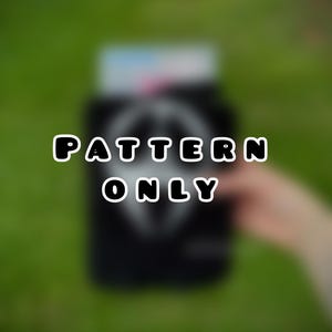 May include: A black object with the words "PATTERN ONLY" in white, outlined letters. The background is a blurred green, suggesting grass or foliage. The object appears to be held by a person.