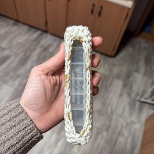 May include: A white and gold crocheted pill case. The case is rectangular with a clear plastic pill organizer inside. The text "Walgreens" is visible on the organizer. The crochet work has a textured appearance.