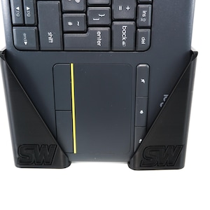 May include: A black keyboard with a built-in touchpad and a yellow accent line. The keyboard is held in place by a black support with the letters "SW" on each side. The keyboard is on a white background.