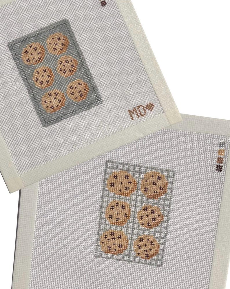 May include: Two square needlepoint canvases featuring cross-stitched designs of cookies on baking sheets. One canvas shows a gray baking sheet with six cookies and the letters MD with a heart. The other shows a grid-patterned sheet with six cookies.