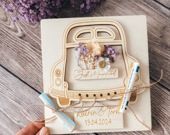May include: A wooden card with a cutout of a car with dried flowers in the back. The card says "Just Married" and "Katrin & Tom 13.04.2024".