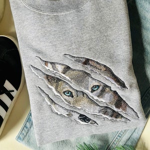 May include: Gray sweatshirt with a ripped design featuring an embroidered wolf's face with blue eyes.