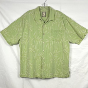 May include: A light green button-down shirt with short sleeves and a leaf pattern. The shirt has a chest pocket and a collar. The fabric has a textured appearance. The shirt is hanging on a hanger.