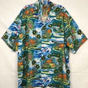 May include: A short-sleeve button-down shirt in a teal blue color featuring a repeating tropical print of palm trees, thatched-roof huts, ocean waves, surfers, and flowers. The shirt has a collared neckline and a single chest pocket on the left.
