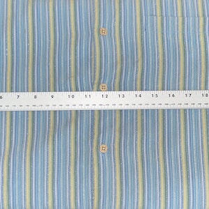 Puede incluir: Camisa abotonada a rayas azules y amarillas con bolsillo en el pecho. La camisa se mide con una regla, mostrando un ancho de aproximadamente 63,5 cm. La camisa tiene un estilo cl&aacute;sico e informal.