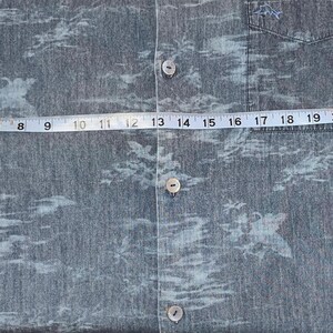 Może przedstawiać: Niebieska koszula zapinana na guziki z tropikalnym nadrukiem. Koszula jest mierzona taśmą mierniczą, pokazując szerokość około 71 cm. Koszula ma kieszeń na lewej piersi i kr&oacute;tkie rękawy.