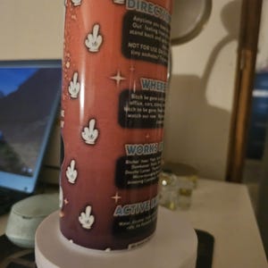 Puede incluir: Un recipiente cil&iacute;ndrico con fondo rojo y gestos de manos blancos. El recipiente tiene texto que dice "DIRECTIO", "NOT FOR USE ON", "WHERE", "WORKS" y "ACTIVE IN".