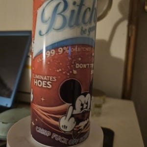 Puede incluir: Un vaso cil&iacute;ndrico con un dise&ntilde;o degradado rojo y marr&oacute;n. El vaso presenta el texto "Bitch be gone" y "Eliminates hoes". Un rat&oacute;n de dibujos animados est&aacute; mostrando el dedo medio. Tambi&eacute;n es visible el texto "Crisp fuck off scum".