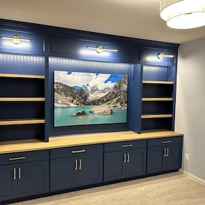 Könnte beinhalten: Ein eingebautes Entertainment-Center mit blauer Lackierung und Holzregalen. Das Center verfügt über ein großes gerahmtes Landschaftsfoto eines Bergsees und eine Reihe blauer Schränke mit goldener Beschläge.