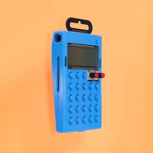 Puede incluir: Un operador de bolsillo azul impreso en 3D con una pequeña pantalla LCD, botones rojos y una cuadrícula de botones. El texto "pocket operator" está impreso en el dispositivo.