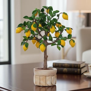 May include: A small potted lemon tree with bright yellow lemons and green leaves. The tree is in a decorative beige pot and sits on a dark brown wooden table with gold-colored legs. A teacup and books are also on the table.