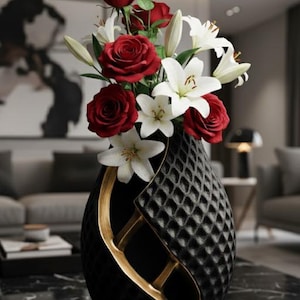 May include: A black vase with a quilted pattern and gold accents holds a bouquet of red roses and white lilies. The vase has a unique, elegant shape, and the flowers add a vibrant contrast.
