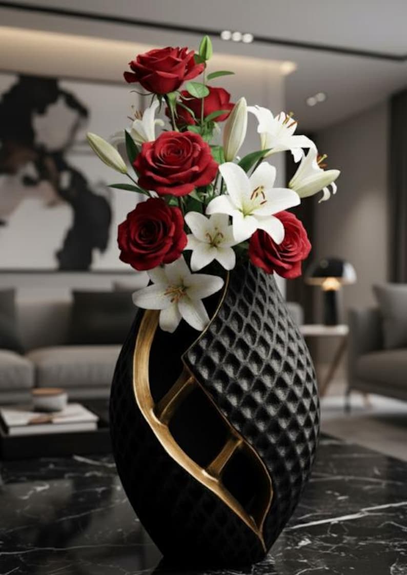 May include: A black vase with a quilted pattern and gold accents holds a bouquet of red roses and white lilies. The vase has a unique, elegant shape, and the flowers add a vibrant contrast.