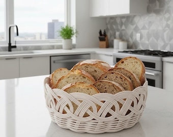 Op de afbeelding: Een witte, geweven broodmand gevuld met gesneden brood. De broodschijfjes variëren in kleur van licht- tot donkerbruin. De mand staat op een wit aanrecht in een moderne keuken.