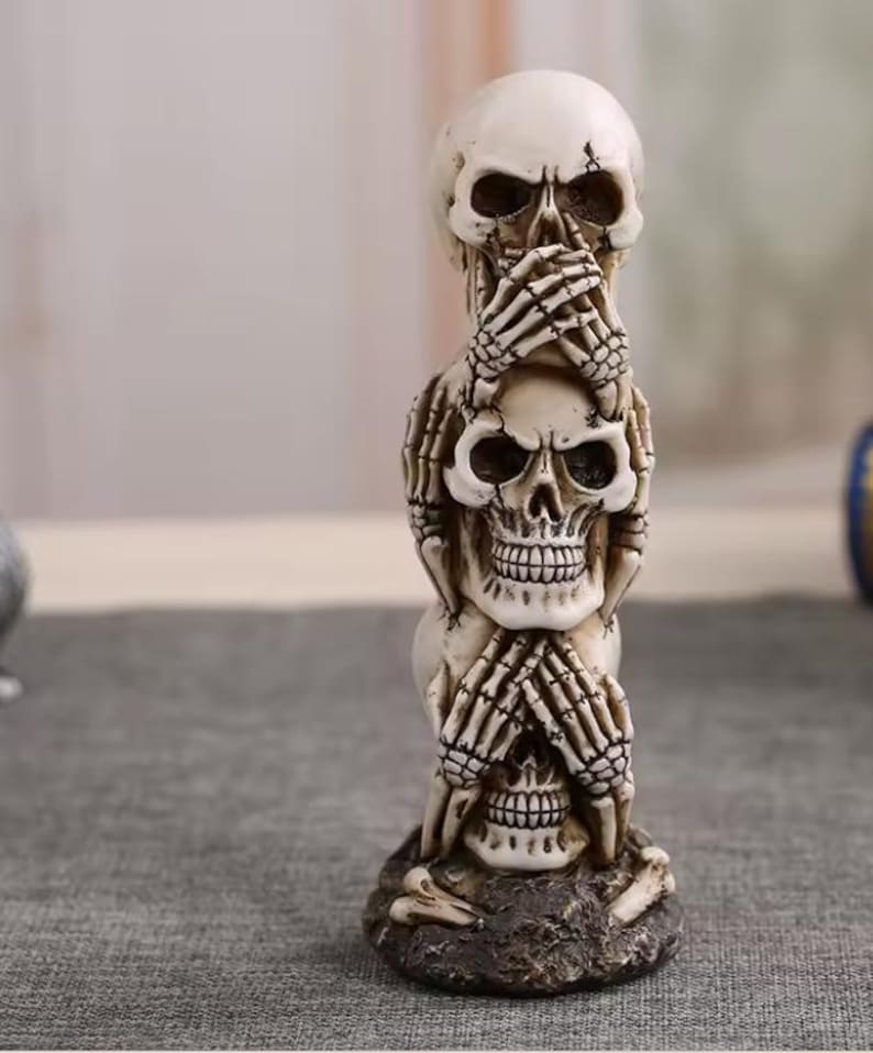 K&ouml;nnte beinhalten: Eine gestapelte Skulptur aus drei Totenk&ouml;pfen, jeder mit einer anderen Handgeste. Der obere Sch&auml;del hat die H&auml;nde &uuml;ber den Augen, der mittlere Sch&auml;del hat die H&auml;nde &uuml;ber dem Mund und der untere Sch&auml;del hat die H&auml;nde &uuml;ber den Ohren. Die Skulptur ist cremefarben und steht auf einem dunklen, strukturierten Sockel.