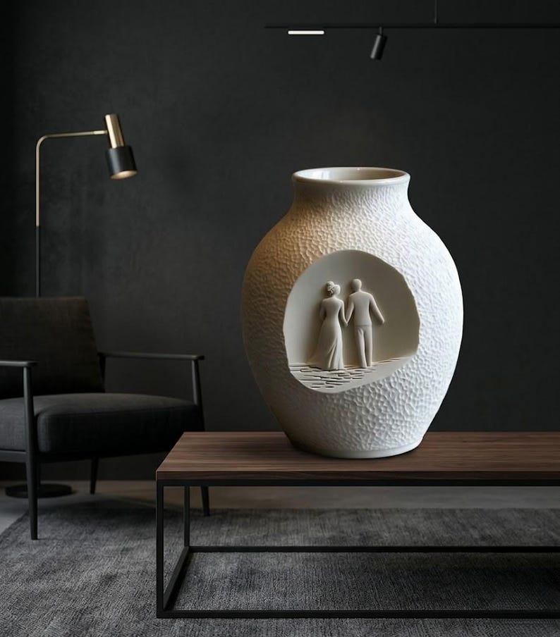 May include: A textured white ceramic vase with a circular cutout revealing a sculpted couple. The vase has a wide base and a narrow neck. The couple is depicted in a wedding scene. Home decor.