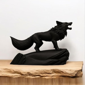 May include: A black sculpture of a wolf standing on a rock formation. The wolf is depicted with its mouth open, as if howling. The sculpture is placed on a wooden surface against a white background. The wolf's fur is detailed, and the sculpture has a matte finish.