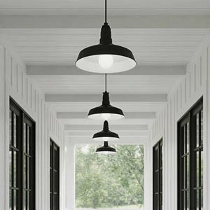 May include: A series of black pendant lights with white interiors hang from the ceiling in a white hallway. The lights are evenly spaced and create a sense of depth. The hallway has white walls and black framed windows.