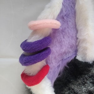 Könnte beinhalten: Ein plüschiges Einhorn-Ohr in Lila, Weiß und Schwarz. Das Ohr hat ein rosa Horn und lila und rote Akzente. Das Design ist weich und skurril, perfekt für Cosplay oder Kostüme.