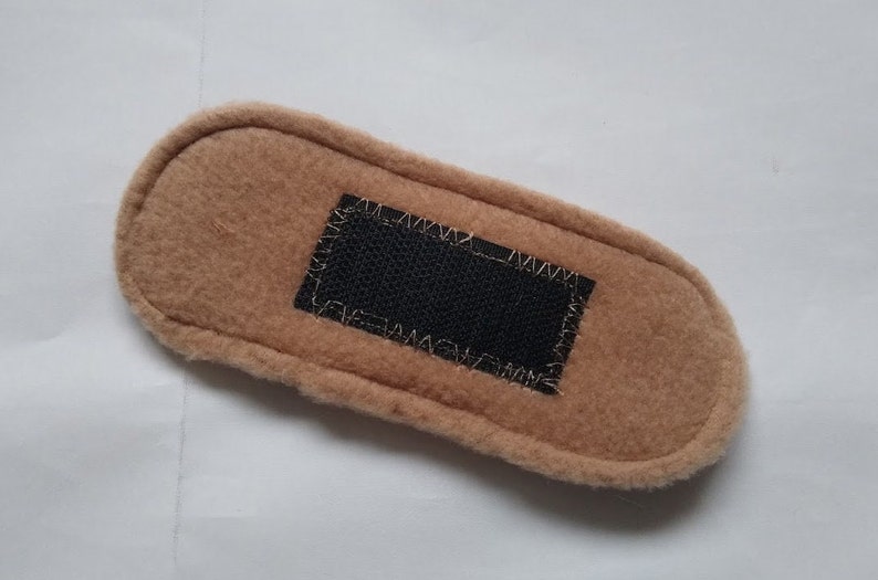 May include: A brown fleece fabric rectangle with a black velcro patch sewn in the center.