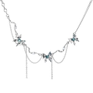 May include: Silver-toned necklace featuring butterfly pendants with teal accents and dangling chains. The necklace has a delicate design with small pearl embellishments, creating an elegant and whimsical aesthetic. A perfect accessory for adding a touch of charm.