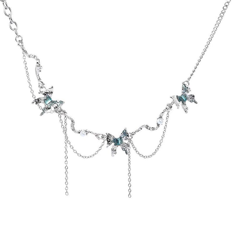 May include: Silver-toned necklace featuring butterfly pendants with teal accents and dangling chains. The necklace has a delicate design with small pearl embellishments, creating an elegant and whimsical aesthetic. A perfect accessory for adding a touch of charm.