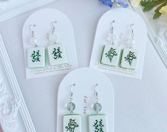 May include: Three pairs of earrings with a white and green design, each featuring a Mahjong tile with Chinese characters and a decorative element. The earrings are displayed on white cards with the text "For You".