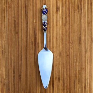 May include: A silver cake server with a decorative handle wrapped in gold wire and accented with blue and white beads.