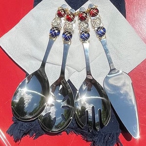 May include: Four silver serving utensils with red, white, and blue glass bead handles. The utensils include a serving spoon, a slotted spoon, a serving fork, and a cake server.
