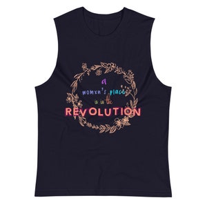Puede incluir: Camiseta sin mangas azul marino con el texto "a womxn's place is in the REVOLUTION" en un diseño de corona floral. El texto está en un degradado de colores, incluyendo morado, rosa y naranja. La camiseta es sin mangas.