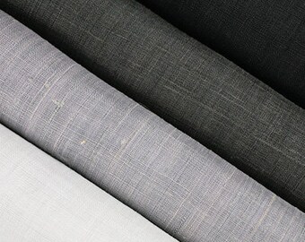 May include: Close-up of several rolls of fabric in shades of white, gray, and black. The fabric has a textured, woven appearance, with visible threads creating a subtle pattern. The rolls are arranged diagonally, showcasing the color variations.