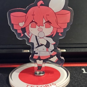 May include: A clear acrylic figure of a cartoon character with red hair and a white and black outfit. The figure is holding a microphone and is mounted on a red and white circular base with the text "TETORIS".