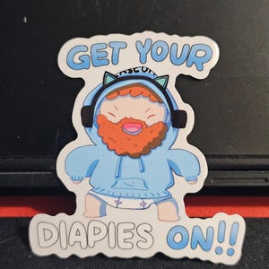 Könnte beinhalten: Ein Aufkleber mit einer Cartoonfigur mit rotem Bart und blauem Kapuzenpullover mit Katzenohren, Kopfhörern und Windel. Der Text "GET YOUR DIAPIES ON!!" steht in Blau darüber und darunter.