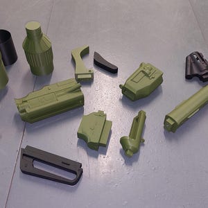 Può includere: Un set di 10 pezzi di plastica stampati in 3D in nero e verde. I pezzi sono di varie forme e dimensioni e sembrano essere pezzi di una pistola giocattolo.