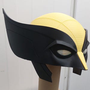 Peut inclure: Un masque de costume en plastique noir et jaune avec une surface texturée. Le masque a une grande zone oculaire noire moulée avec un maillage blanc recouvrant les yeux. Le masque est conçu pour ressembler au personnage Wolverine.