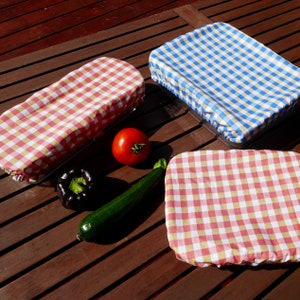 Peut inclure: Trois couvercles de bol rectangulaires en tissu avec des bords élastiques, présentant des motifs vichy rouges et blancs ou bleus et blancs. Une tomate rouge, un poivron violet foncé et une courgette verte sont placés entre les couvercles.